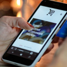 Eine Frau hält ein Handy in der Hand. Auf dem Bildschirm ist ein Online-Shop zu zu sehen.