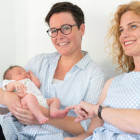 Zwei Frauen sitzen auf einem Sofa. Eine von ihnen hält ein Baby in ihrem Arm.