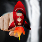 Ein Mann berührt einen Bildschirm, auf welchem ein Bild einer Rakete abgebildet ist.