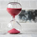 Eine Sanduhr mit rotem Sand steht auf einem Tisch.