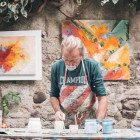 Ein Mann töpfert verschiedene Gefäße. Im Hintergrund hängen drei Kunstwerke.