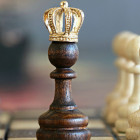 Schachfigur mit einer Krone. Links stehen braune und rechts weiße Figuren.