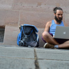 Ein Mann sitzt mit seinem Laptop und seinem Rucksack auf einer Straße.