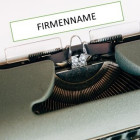 Alte Schreibmaschine mit weißem Blatt Papier. Auf diesem steht Firmenname.
