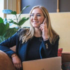 Frau sitzt mit einem Laptop auf einem Sofa und telefoniert.