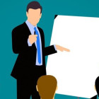 Ein Mann steht vor einem Flipchart und hält einen Vortrag. Es gibt drei Zuschauer.