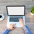Mann sitzt an Tisch mit Homeoffice-Ausstattung und arbeitet am Laptop