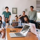 Viele Menschen stehen und sitzen um einen Tisch mit Laptops.