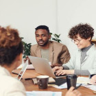 Männer und Frauen sitzen mit Laptops an einem Tisch.