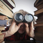 Mann mit Fernglas zwischen Büchern