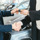 Eine Person überreicht mit der linken Hand einer anderen Person einen Autoschlüssel. Beide schütteln sich die rechte Hand.
