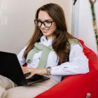 Frau mit Brille sitzt auf einem roten Stuhl mit Laptop auf dem Schoß.