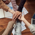 Hände, die sich zusammenschließen und über einem Tisch mit Businessunterlagen die Hand geben.