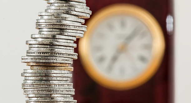 Ein Münzstapel ist vor einer Wanduhr aufgestellt