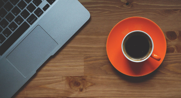 Eine Tasse mit Kaffee steht neben einem Laptop