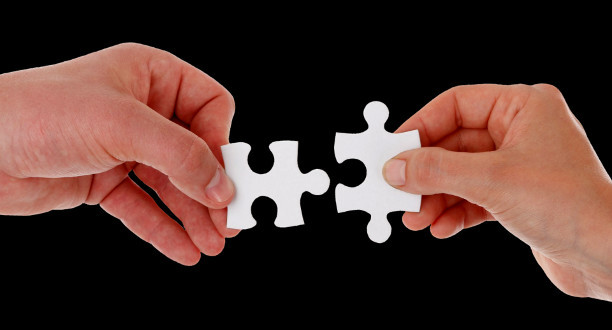 Zwei Menschen halten zwei passende Puzzleteile zueinander