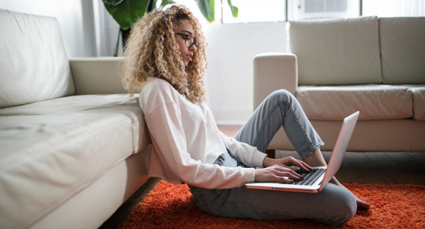 Eine Frau sitzt auf dem Boden mit ihrem Laptop.