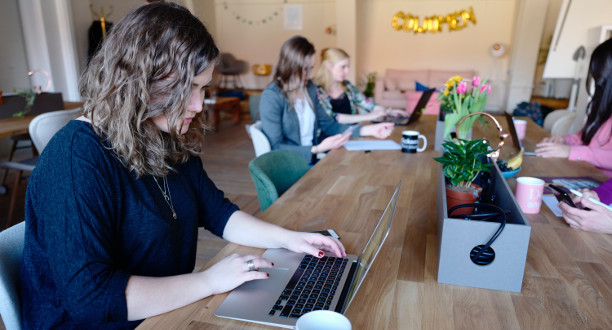 Zwei Frauen sitzen mit ihren Laptops an einem Holztisch.