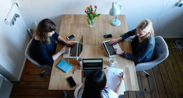Drei Frauen sitzen mit ihren Laptops an einem Tisch.