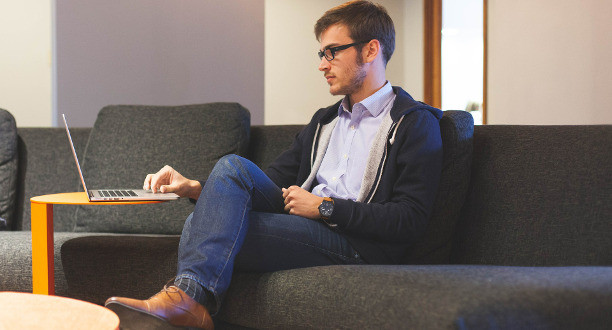 Ein Mann sitzt auf einem Sofa und arbeitet an seinem Laptop.