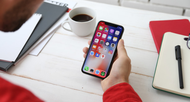 Ein Mann sitzt am Schreibtisch hält ein Handy in der Hand.