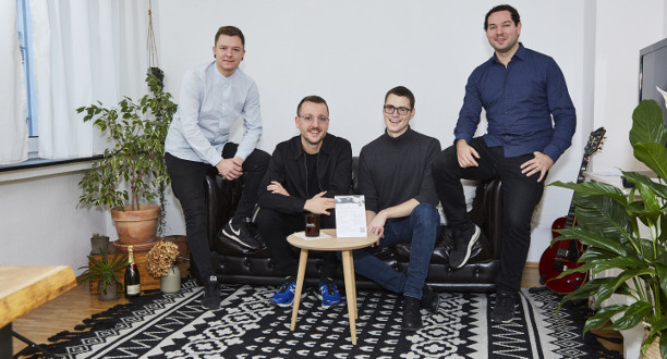 Zwei Männer sitzen auf einem Sofa und zwei weitere sitzen an der Seite.