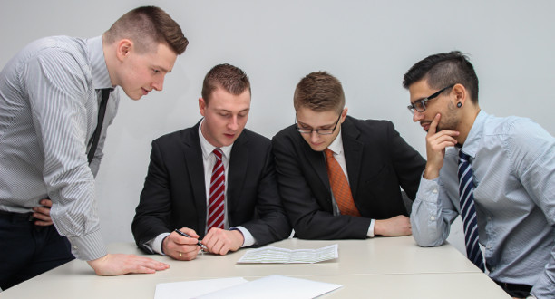 Vier Männer schauen sich einen Zettel an, der auf dem Tisch liegt.
