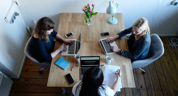 Drei Frauen sitzen an einem Tisch und arbeiten an ihren Laptops.