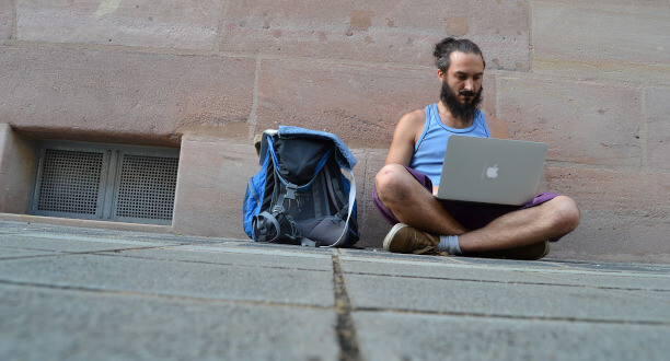 Ein Mann sitzt mit seinem Laptop und seinem Rucksack auf einer Straße.