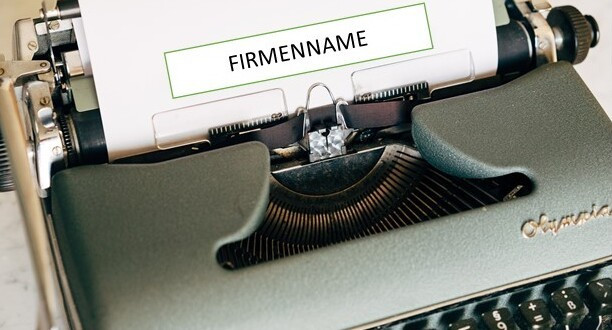 Alte Schreibmaschine mit weißem Blatt Papier. Auf diesem steht Firmenname.