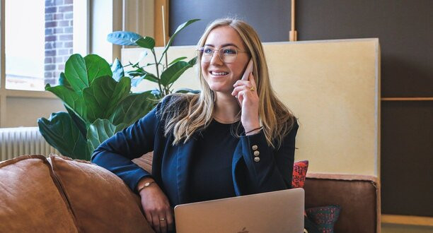 Frau sitzt mit einem Laptop auf einem Sofa und telefoniert.
