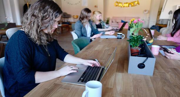 Frau sitzt mit Laptop an einem Tisch.