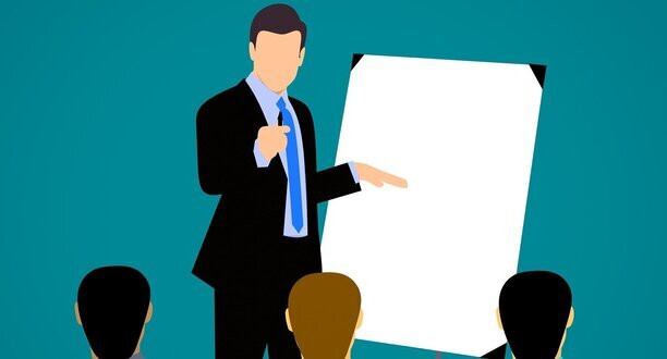 Ein Mann steht vor einem Flipchart und hält einen Vortrag. Es gibt drei Zuschauer.