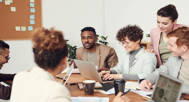 Männer und Frauen sitzen mit Laptops an einem Tisch.