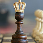 Eine Holzspielfigur mit einer Krone steht auf einem Schachbrett