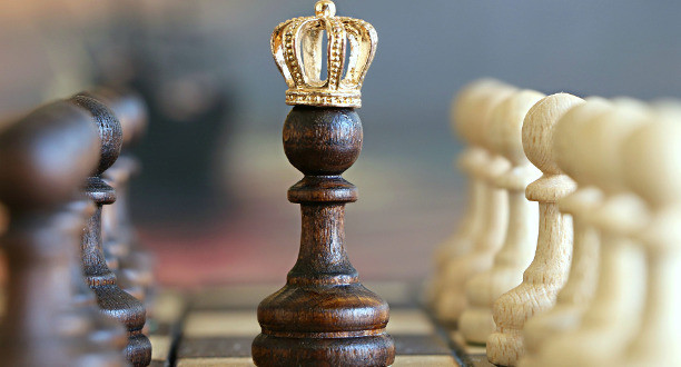 Eine Holzspielfigur mit einer Krone steht auf einem Schachbrett