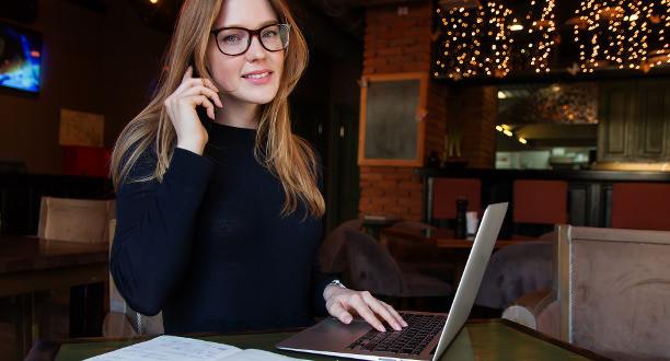 Eine Frau mit roten Haaren und Brille sitzt an einem Laptop.