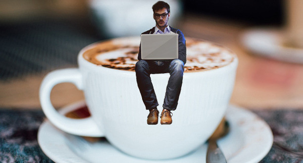 Ein Mann sitzt mit seinem Laptop auf einer Kaffeetasse.