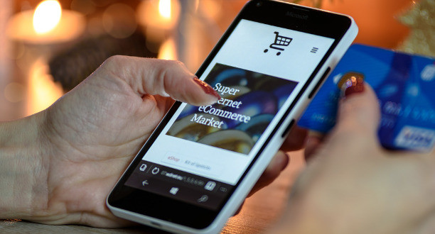 Eine Frau hält ein Handy in der Hand. Auf dem Bildschirm ist ein Online-Shop zu zu sehen.