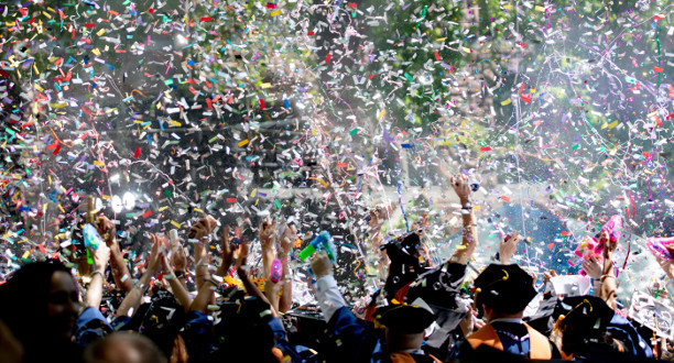 Feiernde Menschen stehen im Vordergrund während in der Luft buntes Konfetti fliegt.