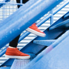 Ein Mensch mit orangenen Schuhen steigt eine blaue Treppe hinauf.