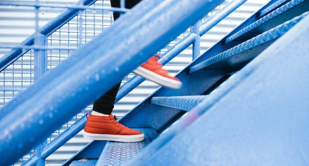 Ein Mensch mit orangenen Schuhen steigt eine blaue Treppe hinauf.
