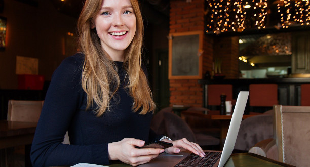 Eine lächelnde Frau sitzt mit ihrem Laptop am Schreibtisch.