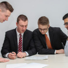 Vier Männer schauen sich einen Zettel an, der auf dem Tisch liegt.