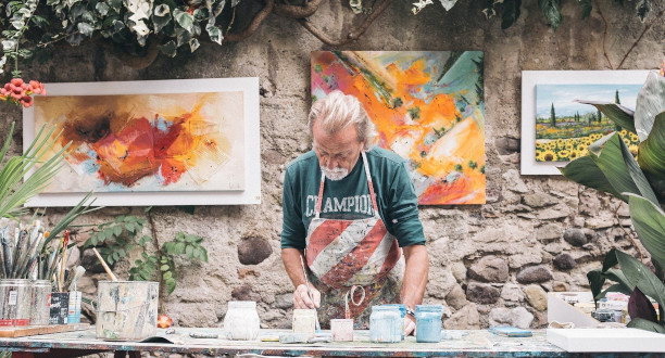 Ein Mann töpfert verschiedene Gefäße. Im Hintergrund hängen drei Kunstwerke.