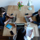 Drei Frauen sitzen an einem Tisch und arbeiten an ihren Laptops.