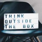 Ein Schild mit der Beschriftung Think outside the box steht auf einem Stuhl.