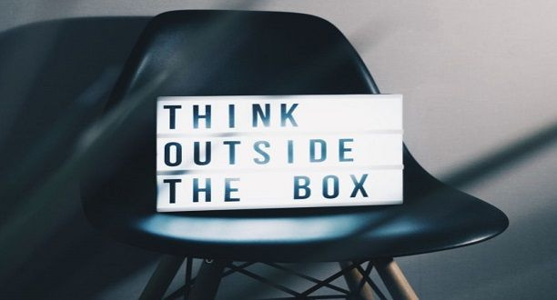 Ein Schild mit der Beschriftung Think outside the box steht auf einem Stuhl.