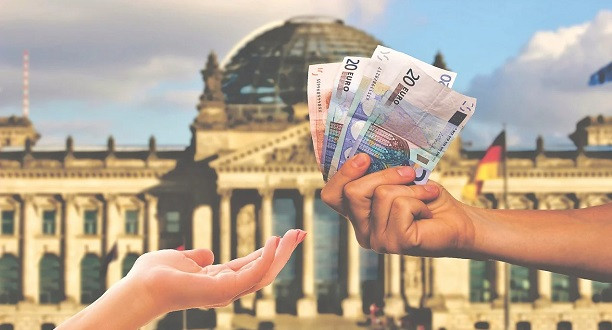 Zwei Hände vor einem Reichstagsbild. Die rechte Hand hält mehrere Geldscheine.