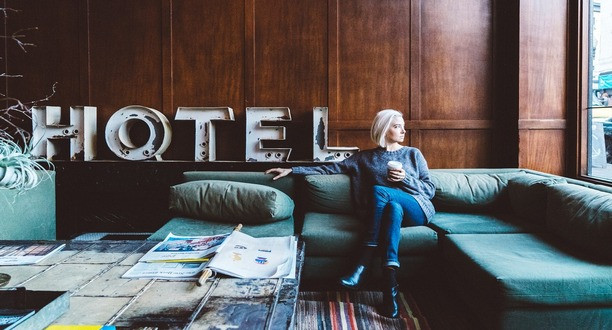 Frau sitzt auf einem Sofa. Im Hintergrund stehen die Buchstaben HOTEL.